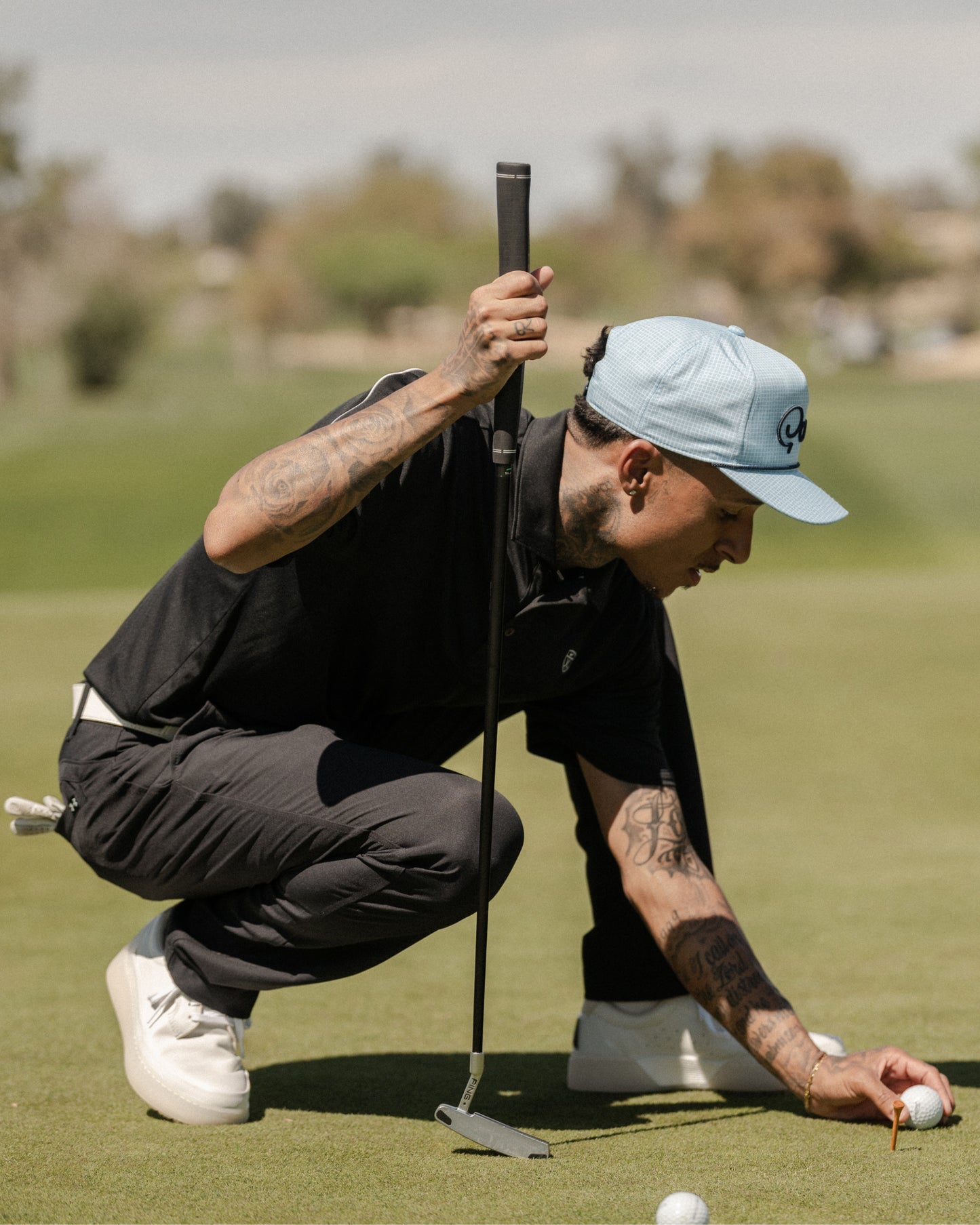 Golfer crouching on a green placing a ball, wearing white and grey Beta Lite golf shoes
