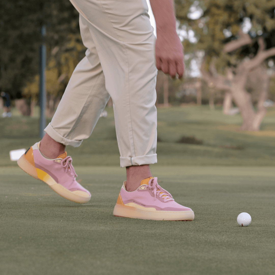 Lavender and orange Beta Lite golf shoe walking toward a golf ball on the putting green