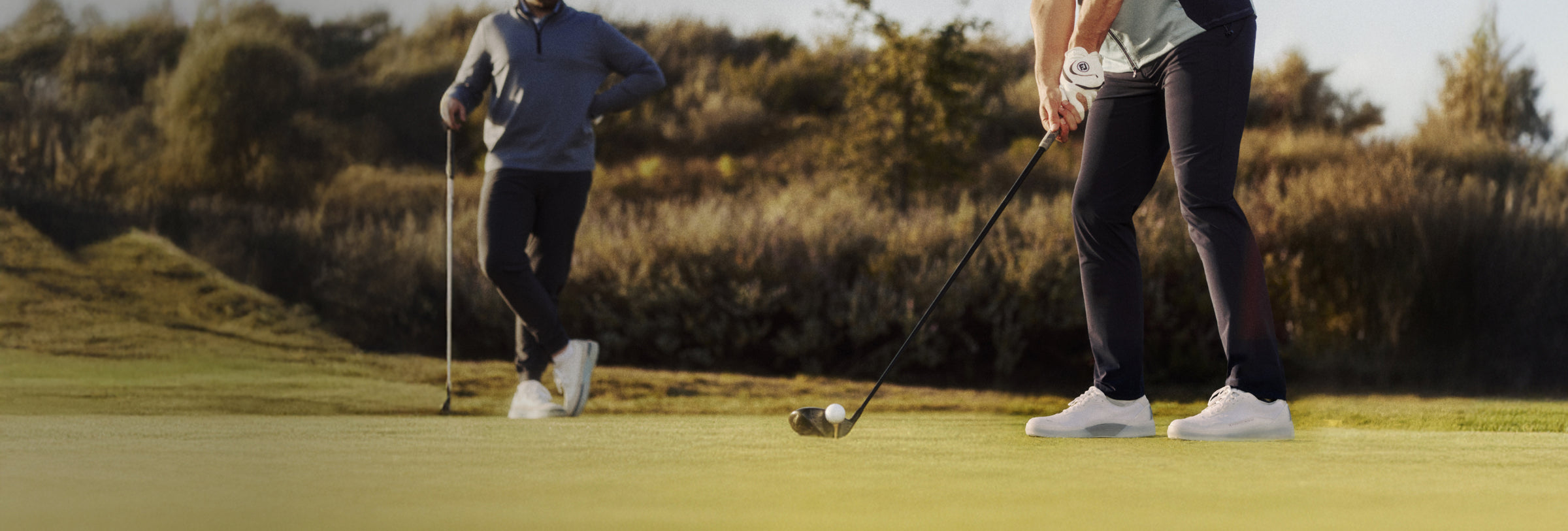 Two golfers on a golf course with a scenic background wearing Beta Lite and Beta Longwing