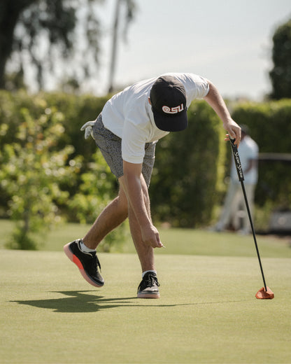 Golfer bending on a green preparing a putt, wearing black and flare Beta Lite golf shoes
