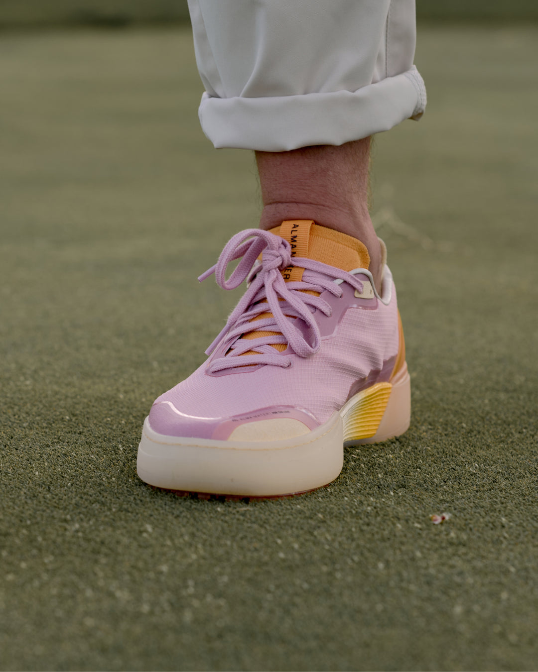 Person wearing a Lavender-Orange golf shoes with yellow accents on a grassy surface
