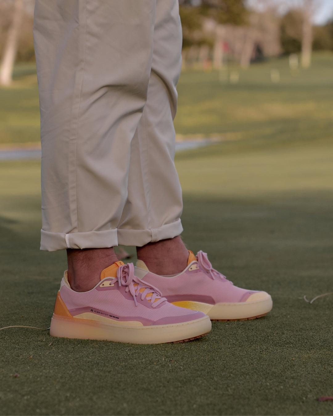 Person wearing Lavender-Orange BEta Lite golf shoes with orange/yellow accents on a grassy field.