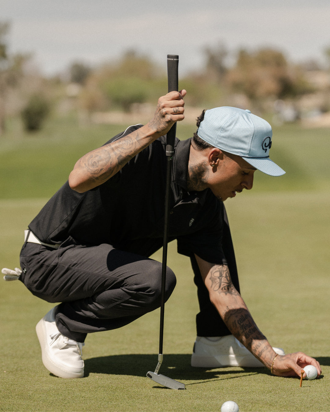 Golfer crouching on a green placing a ball, wearing white and grey Beta Lite golf shoes