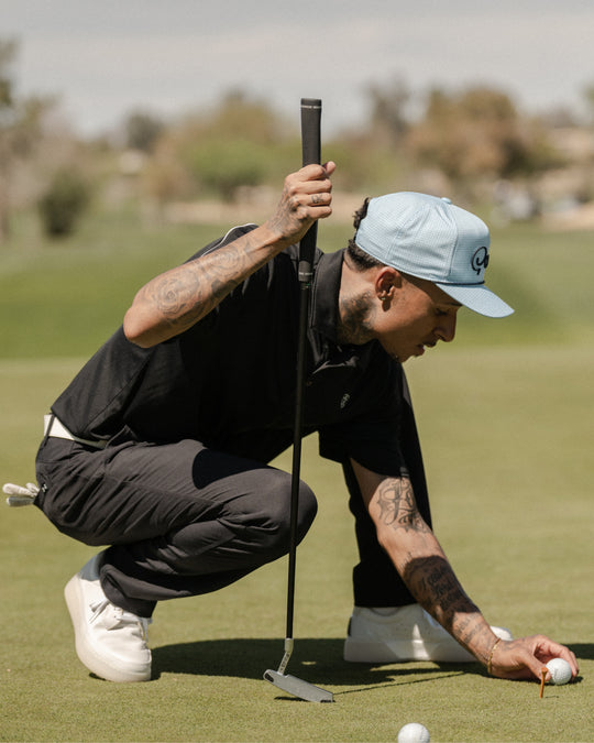 Golfer crouching on a green placing a ball, wearing white and grey Beta Lite golf shoes