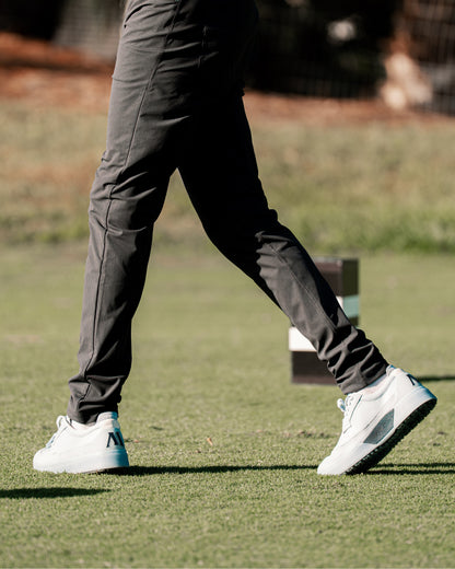 Close-up of person walking on a golf course wearing sky/navy Beta Longwing golf shoes with outsole visible