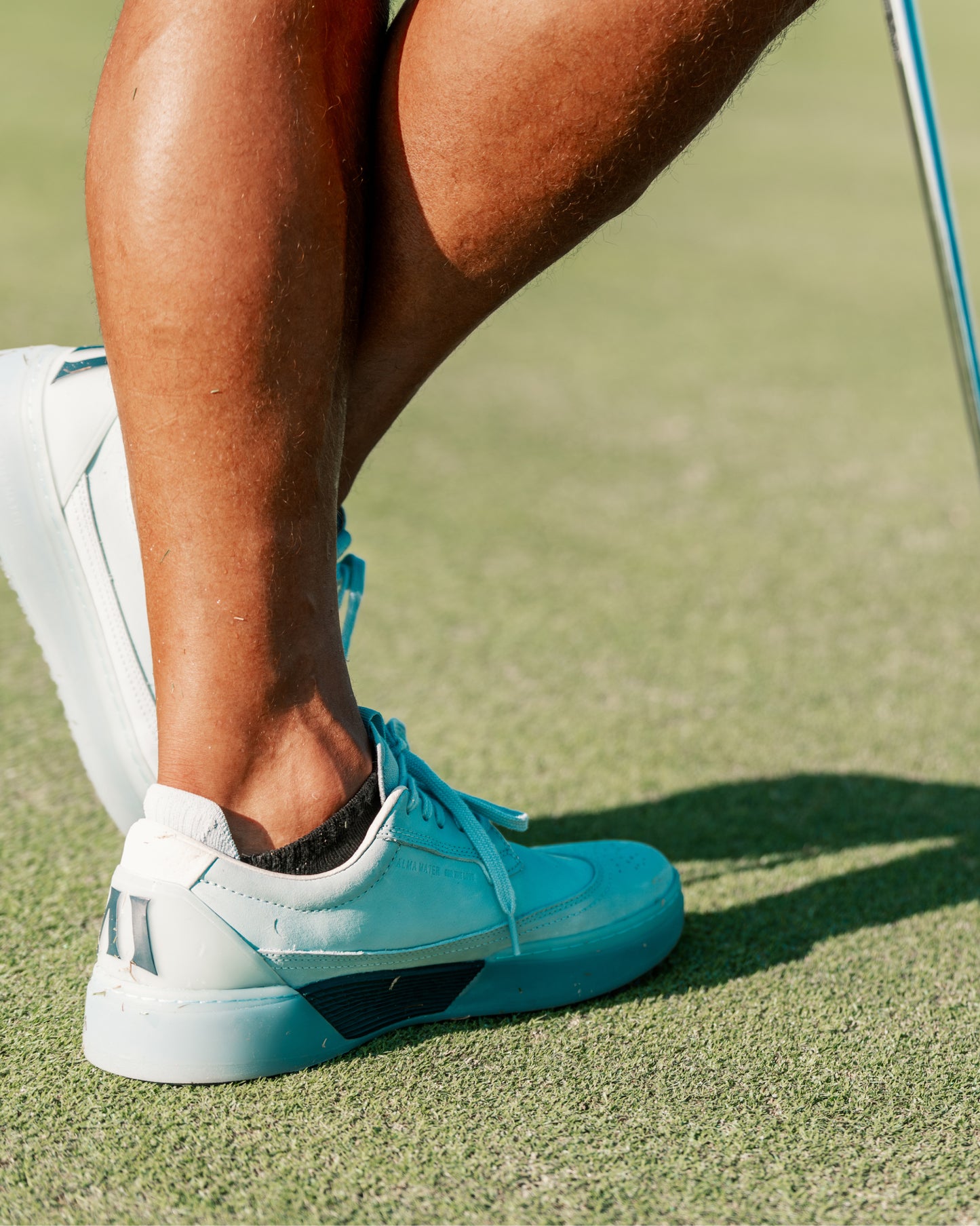 Close-up of person walking on a golf course wearing sky and navy Beta Longwing golf shoes with outsole visible