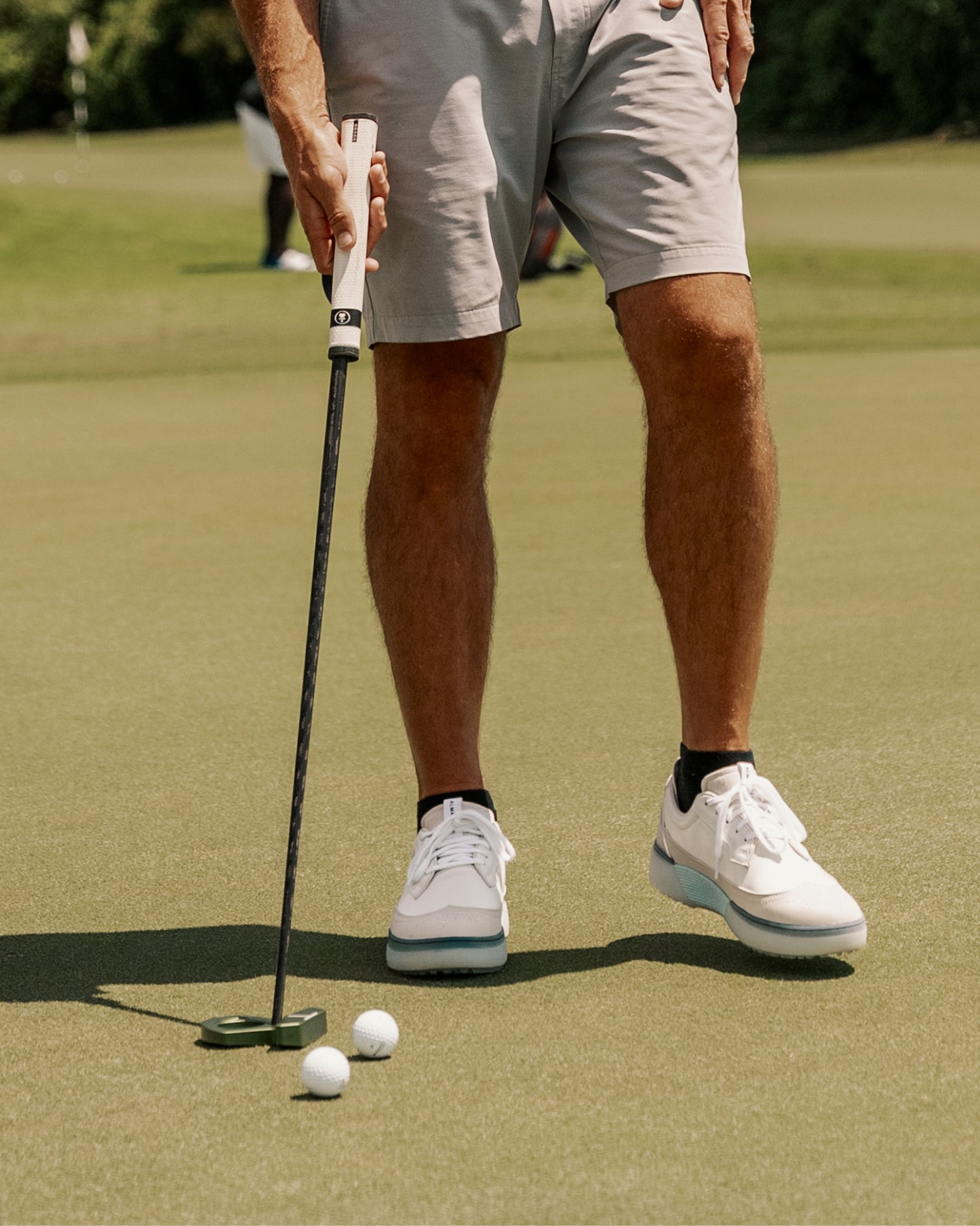 Close-up of golfer putting on a green with golf balls nearby, wearing white and navy Beta Longwing golf shoes