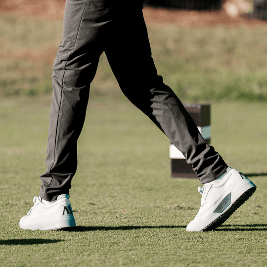Person wearing gray pants and white Beta Longwing golf shoes on a grassy field