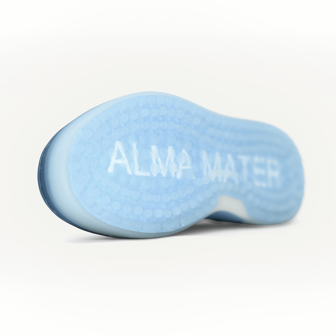 Close-up studio view of the translucent blue spikeless outsole, featuring textured traction pattern and subtle ALMA MATER branding visible through the sole.