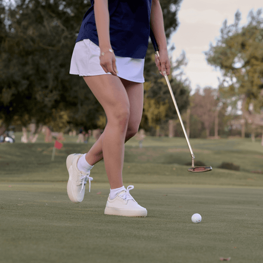 Women’s Beta Derby all-white golf shoe walking across the putting green, lightweight leather golf shoe with spikeless outsole.