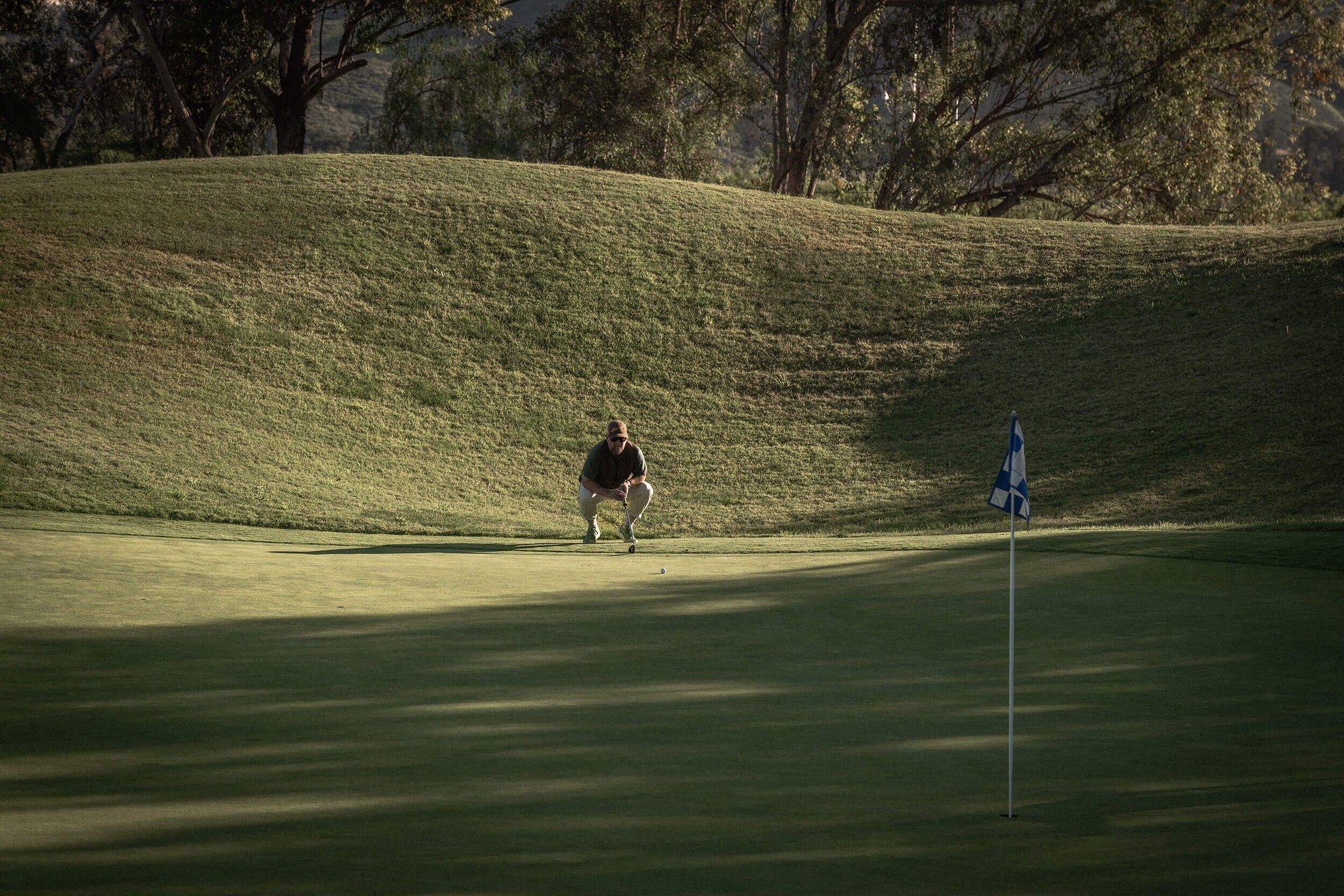 Golfer reading a putt on green wearing Alma Mater M Beta Lite Olive/Aqua golf shoes