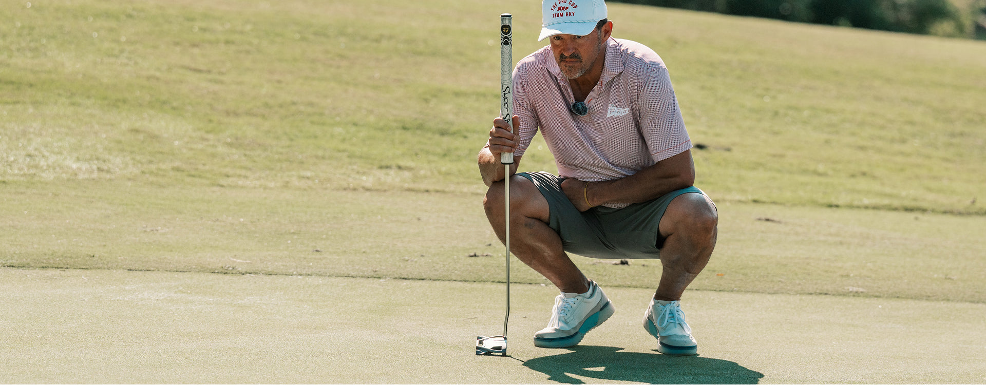 Golfer crouching to read a putt wearing Alma Mater M Beta Longwing golf shoes in white and navy