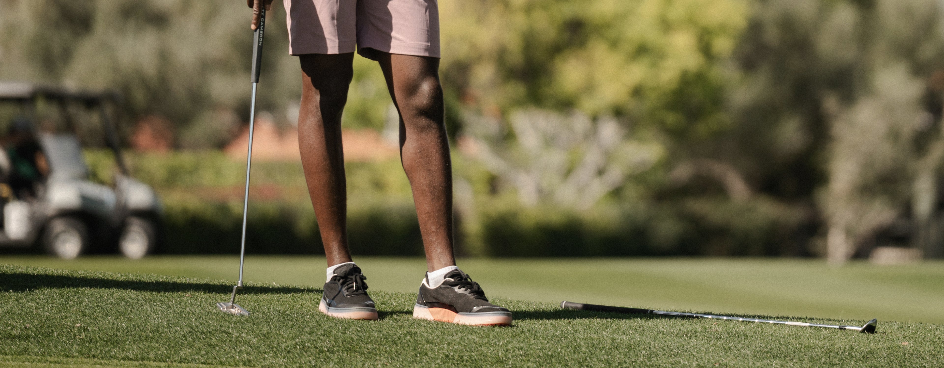 Person on a golf course holding a golf club wearing Black/Flare Beta Lite shoes