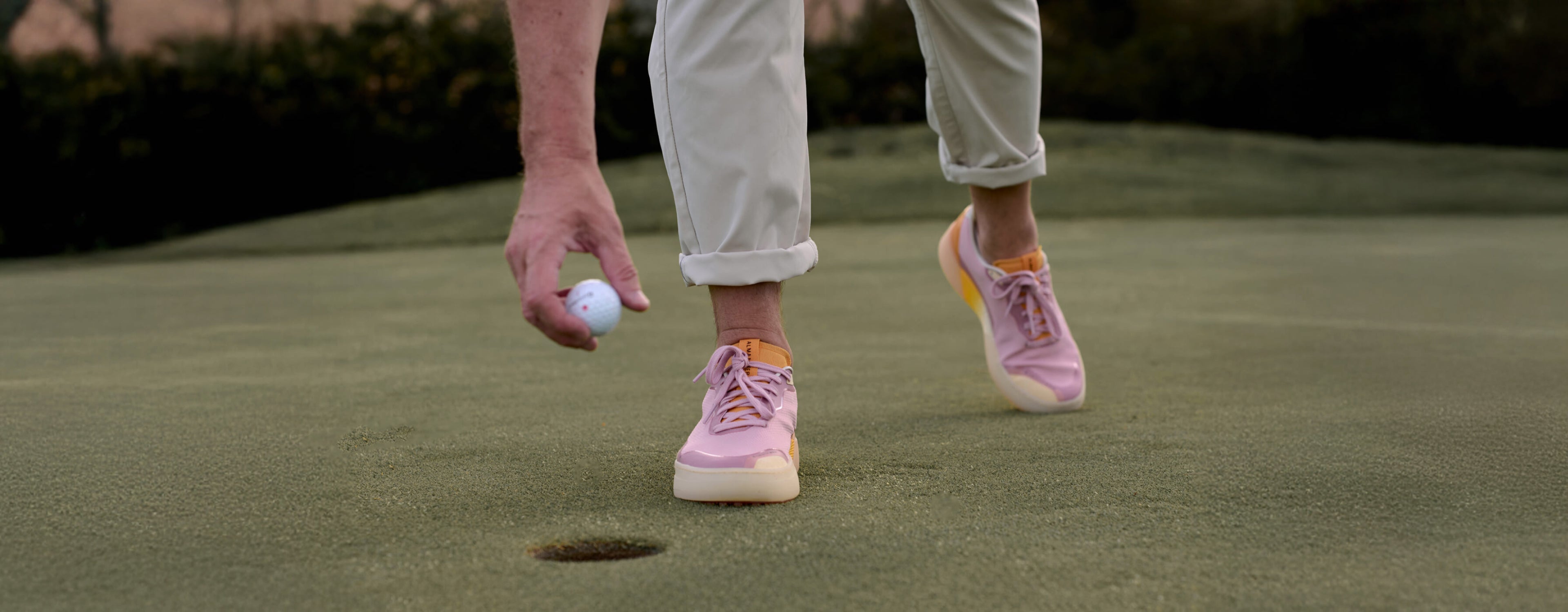 Person on a golf course with Beta Lite Lavender Orange Beta Lite shoes and a golf ball.