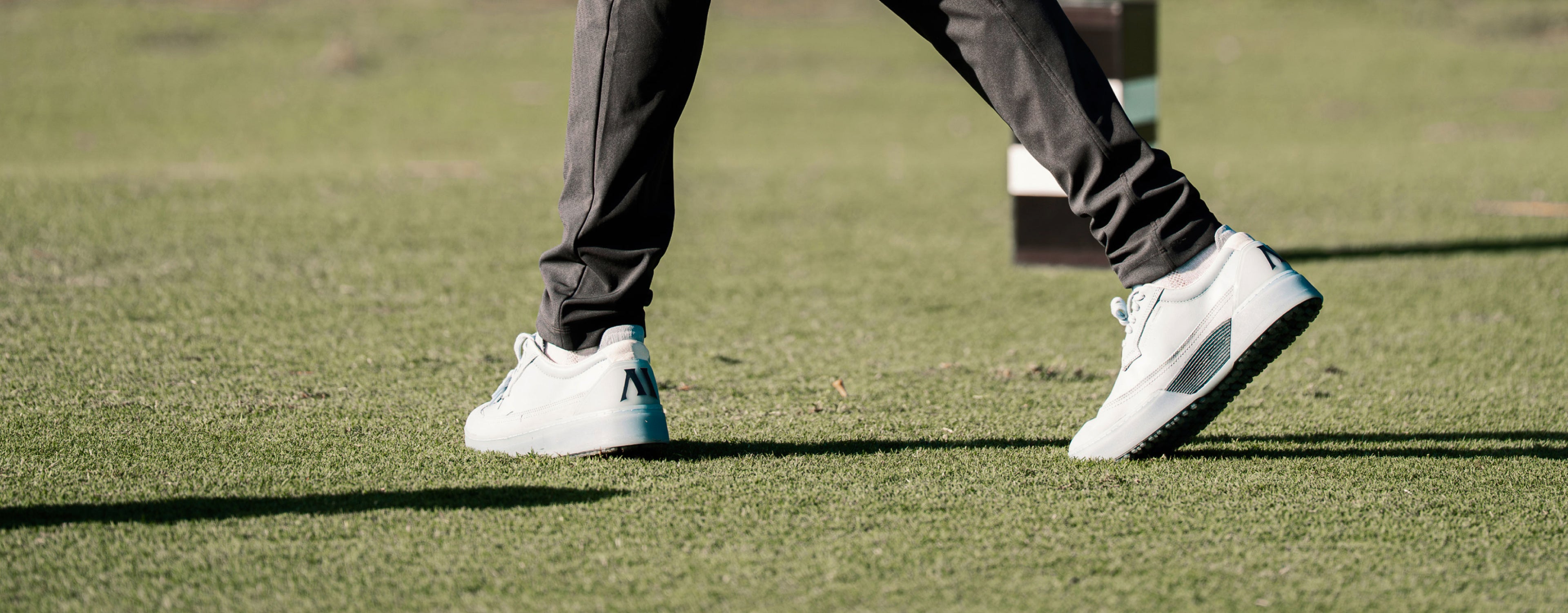 Person walking on a golf course wearing sky and navy Beta Longwing golf shoes